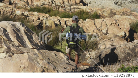 Traversing hiker using trekking poles across rocky hill, with backpack, mat, baseball cap and boots Traversing hiker using trekking poles across rocky hill, with backpack, mat, baseball cap and boots 139258975