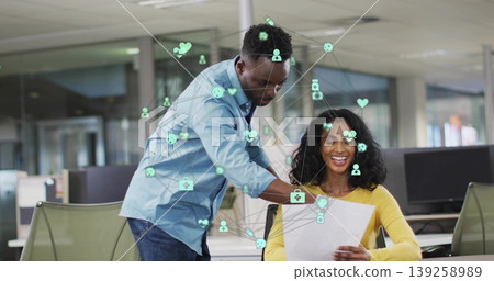 Leaning man pointing at printed document in open-plan office, with monitors, network icon overlays Leaning man pointing at printed document in open-plan office, with monitors, network icon overlays 139258989