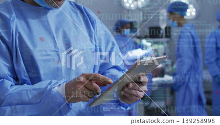 Reviewing surgeon in blue gown holding tablet in operating room, with monitors, surgical lights Reviewing surgeon in blue gown holding tablet in operating room, with monitors, surgical lights 139258998