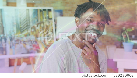 Standing man wearing gray t-shirt examining cityscape painting on easel in studio, with lens flares Standing man wearing gray t-shirt examining cityscape painting on easel in studio, with lens flares 139259002