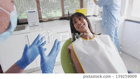 Patient reclining in dental chair in exam room, with dentist gesturing and assistant adjusting lamp Patient reclining in dental chair in exam room, with dentist gesturing and assistant adjusting lamp 139259009
