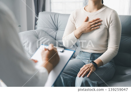 Mental health counseling concept with woman placing hand on chest while talking to therapist during session at home, showing emotional awareness, trust, communication, reflection and support. 139259047