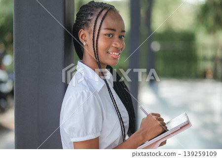 Young African business woman writing on tablet with stylus while standing outdoors, concept of digital planning, paperless work, mobile productivity and modern professional lifestyle. Young African business woman writing on tablet with stylus while standing outdoors, concept of digital planning, paperless work, mobile productivity and modern professional lifestyle. 139259109