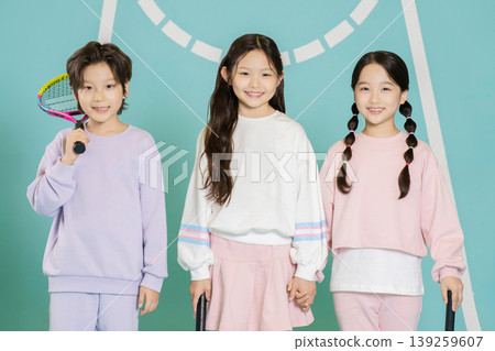 Three children stand together in a sports area. They hold rackets and smile at the camera. They wear colorful sports outfits and seem happy to be with friends. Three children stand together in a sports area. They hold rackets and smile at the camera. They wear colorful sports outfits and seem happy to be with friends. 139259607