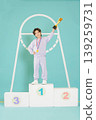 A child stands proudly on the first place podium holding a trophy. The child wears a medal and a pink outfit. The setting shows a simple and fun background with bright colors. 139259731
