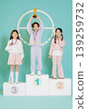 Three children stand on a podium after a sports event. One child holds a trophy on the first place spot, while others show their medals. They smile in a gym setting. 139259732