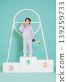 A young athlete stands proudly on a podium after winning a competition. They hold a trophy in one hand and touch their medal with the other. The background has a large hoop design. 139259733