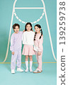 Three kids are standing together, smiling. They are dressed in casual clothing. The background is bright and fun with a simple design. The scene looks lively and energetic. 139259738