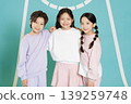 Three kids pose together on a sports court. They wear matching casual outfits and stand close, smiling happily while enjoying their time at a friendly event with friends and family. 139259748