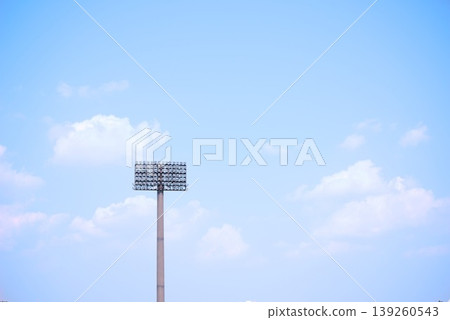 Outdoor lighting towers illuminating stadiums and arenas against a blue sky. Outdoor lighting towers illuminating stadiums and arenas against a blue sky. 139260543