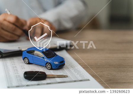 car insurance finance Blue toy car with shield protection icon on insurance policy document with data table and key, hands reviewing paperwork representing approved car insurance coverage verification car insurance finance Blue toy car with shield protection icon on insurance policy document with data table and key, hands reviewing paperwork representing approved car insurance coverage verification 139260623