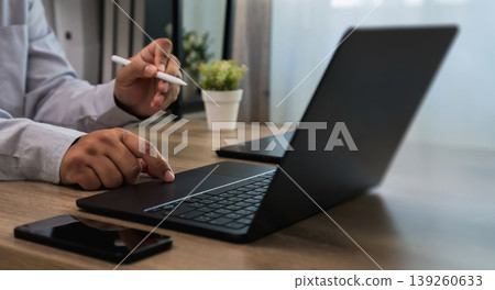 Hands using laptop keyboard and stylus on desk with smartphone and plant, interacting with touchpad and typing workflow for digital communication and online work process with copy space background. 139260633