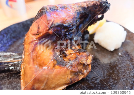 A fragrant grilled fish collar served on a black plate. A fragrant grilled fish collar served on a black plate. 139260945