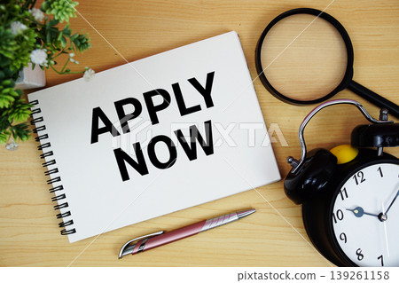 Apply Now text written on notepad with alarm clock and magnifying glass flat lay on wooden background 139261158