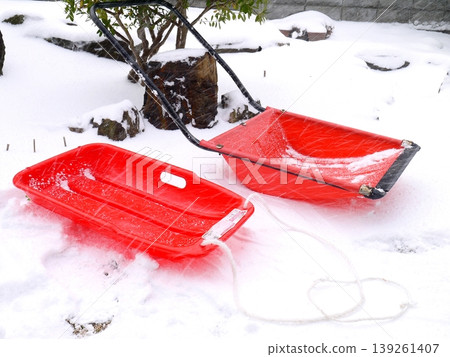 A red sled and a snow shovel are placed on top of the accumulated snow. A red sled and a snow shovel are placed on top of the accumulated snow. 139261407