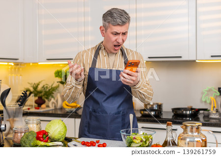 Middle-aged man reading bad smartphone message in kitchen feeling defeat failure and serious problem Middle-aged man reading bad smartphone message in kitchen feeling defeat failure and serious problem 139261759