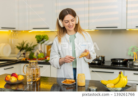 Middle-aged woman dancing to music while making healthy fresh breakfast toast in own kitchen indoors Middle-aged woman dancing to music while making healthy fresh breakfast toast in own kitchen indoors 139261766