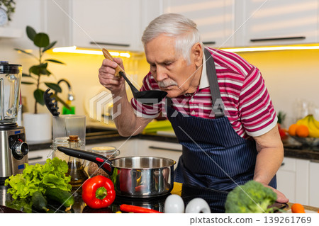 Senior old man tasting fresh soup in home kitchen smiling while cooking healthy diet dinner recipe Senior old man tasting fresh soup in home kitchen smiling while cooking healthy diet dinner recipe 139261769