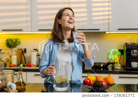 Young woman pouring cold lemon water in home kitchen to quench thirst for diet hydration fit routine Young woman pouring cold lemon water in home kitchen to quench thirst for diet hydration fit routine 139261771