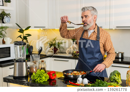 Middle-aged man seasoning tasting vegetables on electric stove in home kitchen for healthy diet meal Middle-aged man seasoning tasting vegetables on electric stove in home kitchen for healthy diet meal 139261778