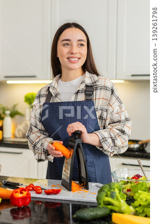 Woman grating fresh carrot on kitchen grater for healthy salad or smoothie preparation at home 139261798