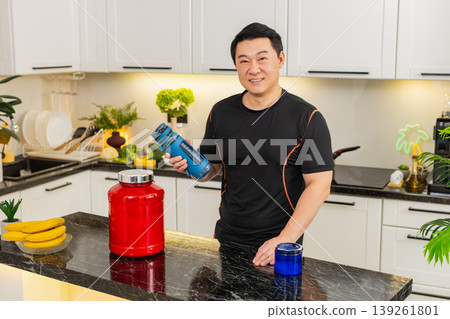 Asian young adult man shaking shaker bottle mixing healthy sports supplement drink in home kitchen Asian young adult man shaking shaker bottle mixing healthy sports supplement drink in home kitchen 139261801