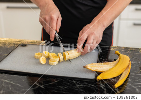Young man putting banana pieces into blender in home kitchen preparing healthy smoothie drink Young man putting banana pieces into blender in home kitchen preparing healthy smoothie drink 139261802