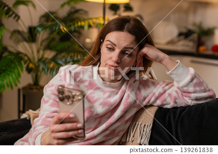 Adult woman doomscrolls smartphone news at night bored tired stressed demotivated mood sighs alone 139261838