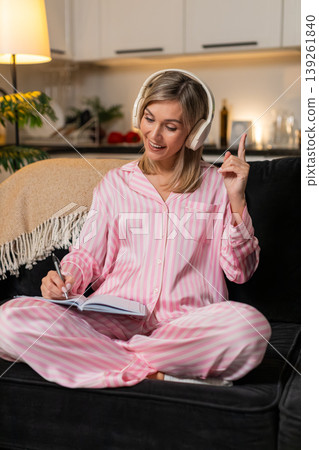 Adult woman in headphones meditation playlist breathes calm eyes closed then writes idea in notebook 139261840
