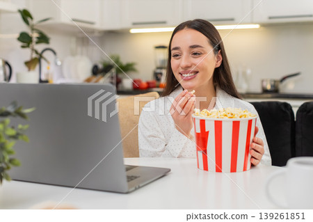 Young woman laughs at movie trailer eats popcorn laptop nearby fun mood entertainment night clip big Young woman laughs at movie trailer eats popcorn laptop nearby fun mood entertainment night clip big 139261851