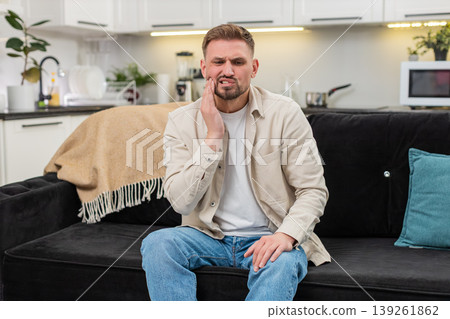 Young man with strong tooth pain covers cheek grimaces massages temple tries to ease sharp ache care Young man with strong tooth pain covers cheek grimaces massages temple tries to ease sharp ache care 139261862