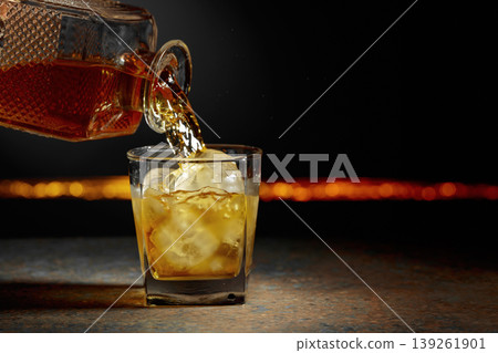 Whiskey is poured from a decanter into a glass with ice. Whiskey is poured from a decanter into a glass with ice. 139261901