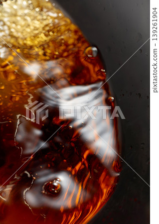 Golden drink is poured into the glass, creating beautiful waves and splashes. 139261904