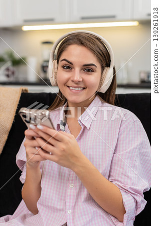 Young woman with wireless headphones nods to music writes idea in smartphone notes and chats online Young woman with wireless headphones nods to music writes idea in smartphone notes and chats online 139261918