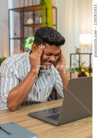 Indian man with laptop suffers headache rubs temples squints at screen needs rest break and relief Indian man with laptop suffers headache rubs temples squints at screen needs rest break and relief 139261933