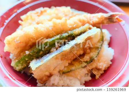 A tempura rice bowl with shrimp tempura and vegetable tempura served in a red bowl. A tempura rice bowl with shrimp tempura and vegetable tempura served in a red bowl. 139261969
