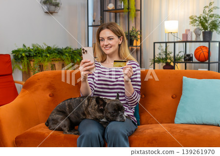Woman with French bulldog at home orders dog food in app on smartphone pays by credit card Woman with French bulldog at home orders dog food in app on smartphone pays by credit card 139261970