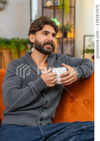 Indian man with hot tea or coffee warms hands gazes out window thoughtful look soft smile calm mood 139261972