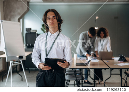 Man is standing and holding notepad. Group of people are working in the office together as a team Man is standing and holding notepad. Group of people are working in the office together as a team 139262120