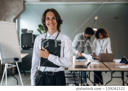 Man is standing and holding notepad. Group of people are working in the office together as a team Man is standing and holding notepad. Group of people are working in the office together as a team 139262122