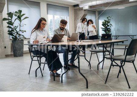 Sitting by the table with laptop. Group of people are working in the office together as a team Sitting by the table with laptop. Group of people are working in the office together as a team 139262222