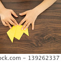 A child's hand folding yellow origami paper 139262337