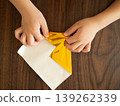 A child's hands folding golden origami on a wooden table. 139262339