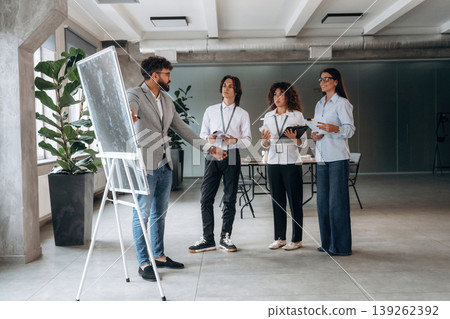 Writing data on the board, explaining stuff. Four office workers are together, employees at work Writing data on the board, explaining stuff. Four office workers are together, employees at work 139262392