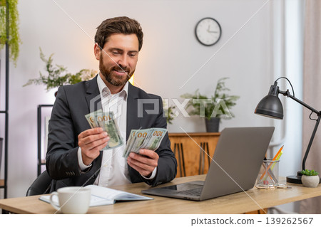 Middle-aged businessman counts cash dollars records budget on laptop writes notes in notebook plans 139262567