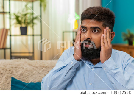 Indian man holds head eyes wide panic overload stress reaction severe pressure mental strain indoors Indian man holds head eyes wide panic overload stress reaction severe pressure mental strain indoors 139262598