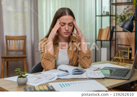 Young woman head in hands staring at overdue bills calculator and laptop wondering how she will pay Young woman head in hands staring at overdue bills calculator and laptop wondering how she will pay 139262610