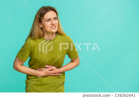 Woman touching belly with painful face expression suffering from cramps, period, or food poisoning Woman touching belly with painful face expression suffering from cramps, period, or food poisoning 139262641