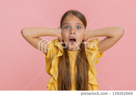 Child girl kid covers ears with hands opens eyes wide showing fear or panic from loud noise or sound 139262669
