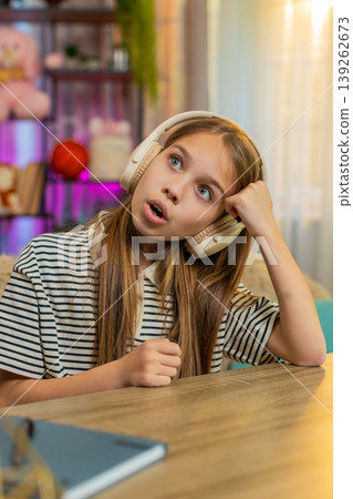 Child girl kid listening to audio fairy tale in headphones at table on home sofa with excitement Child girl kid listening to audio fairy tale in headphones at table on home sofa with excitement 139262673